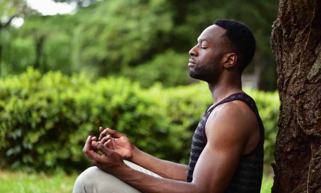 man meditating outside against tree