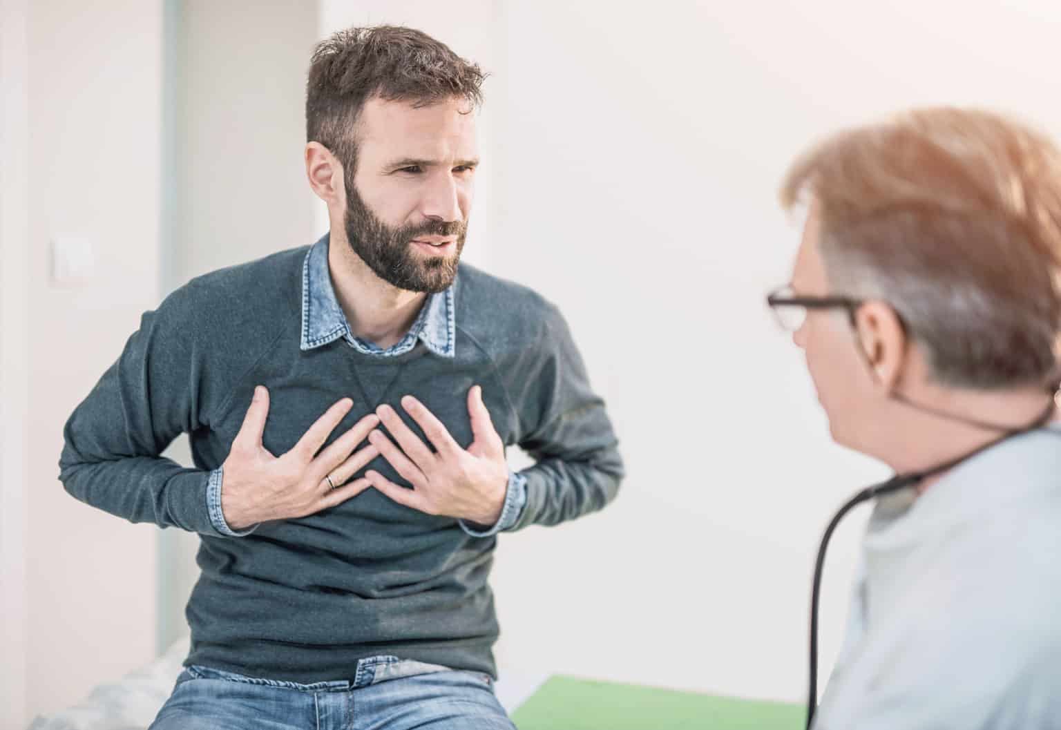 man holding chest talking to doc in clinic