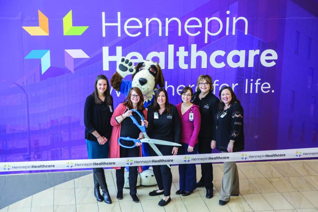 Staff group cutting ribbon in front of Hennepin Healthcare background