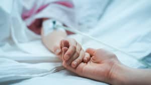 childs hand holding nurses hand in hospital bed, peds tbi, kids with brain injuries, adolescent head trauma, teen head injury, pediatric program for brain injuries