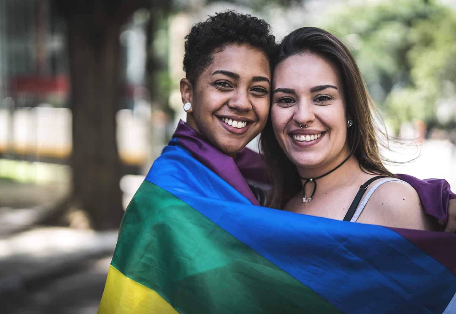 Two Women wrapped in flag atPride Parade Flag, lgbtq+, lgbtq healthcare, transgender, gender-nonconforming, gender and sexual health, gender & sexual health