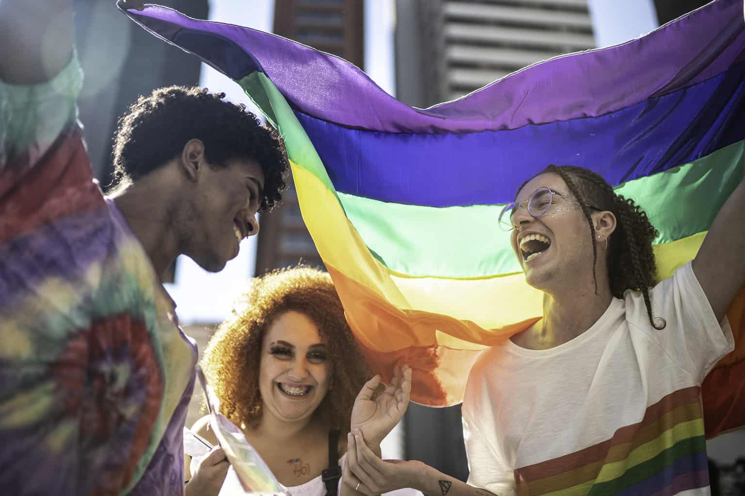 Three Pride Parade Participants with rainbow Flag