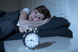 woman looking at clock in bed who needs sleep tips on how to get to sleep and know wind down before bed meaning