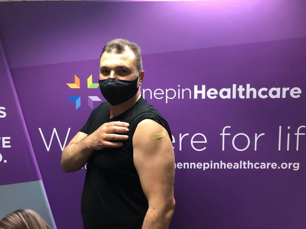 masked employee showing their arm where he got the vaccine