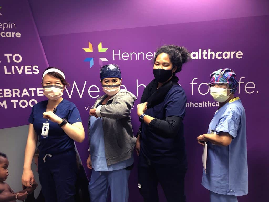 four masked employees showing their arm where they got the vaccine