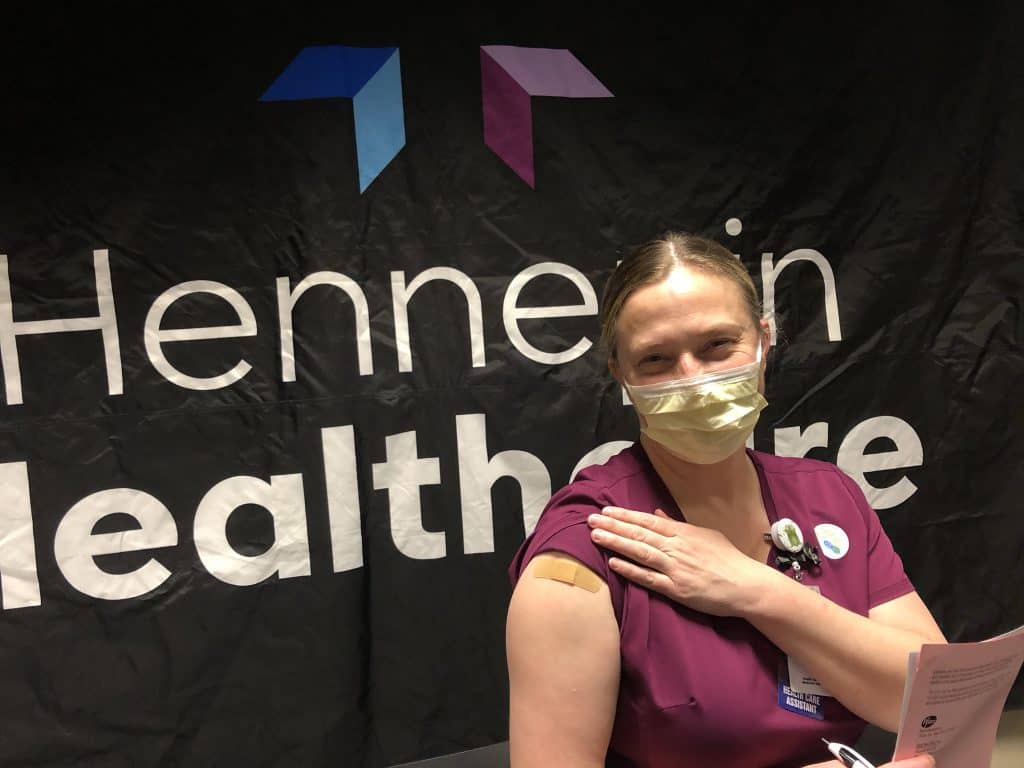 masked employee showing their arm where she got the vaccine