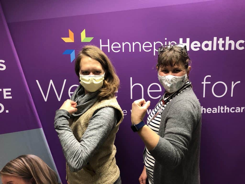 two masked employees showing their arm where they got the vaccine
