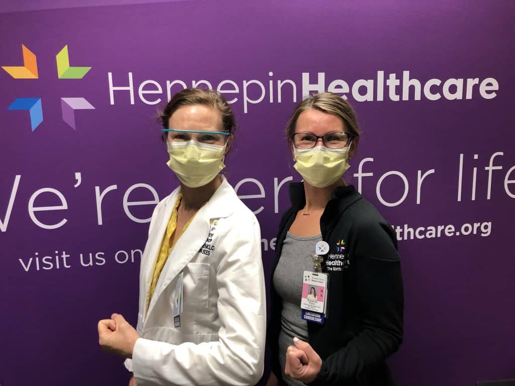 two masked employees showing their arm where they got the vaccine