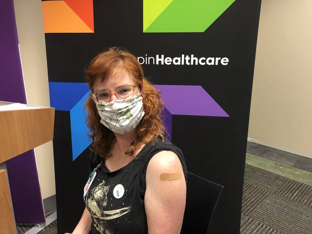 masked employee showing their arm where she got the vaccine