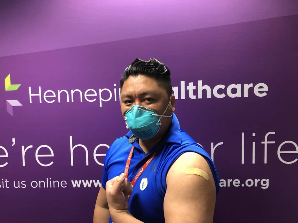 masked employee showing their arm where he got the vaccine