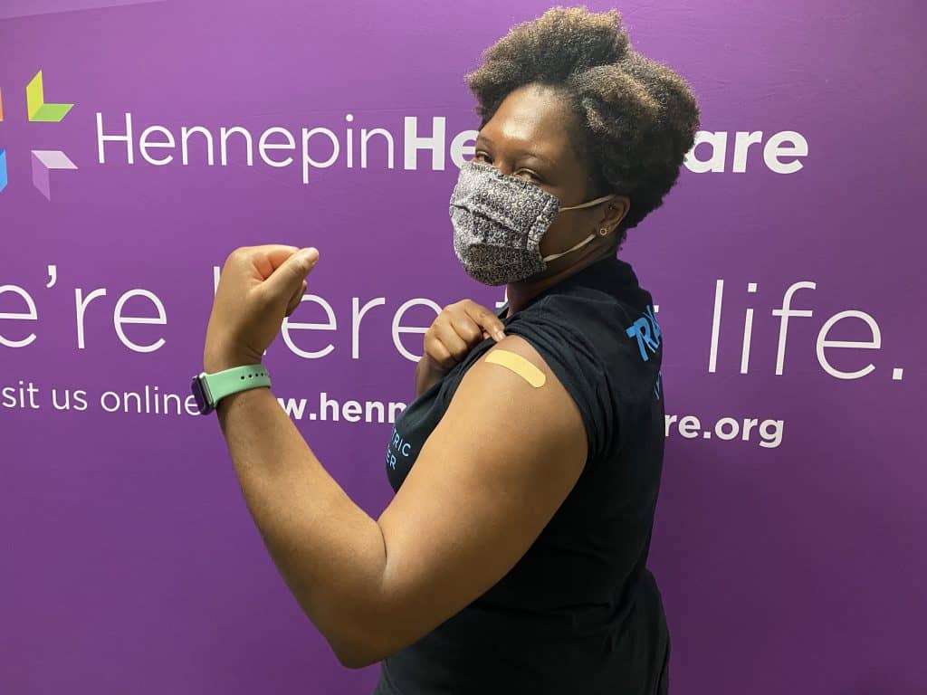 employee wearing mask holding up arm where she had her vaccine