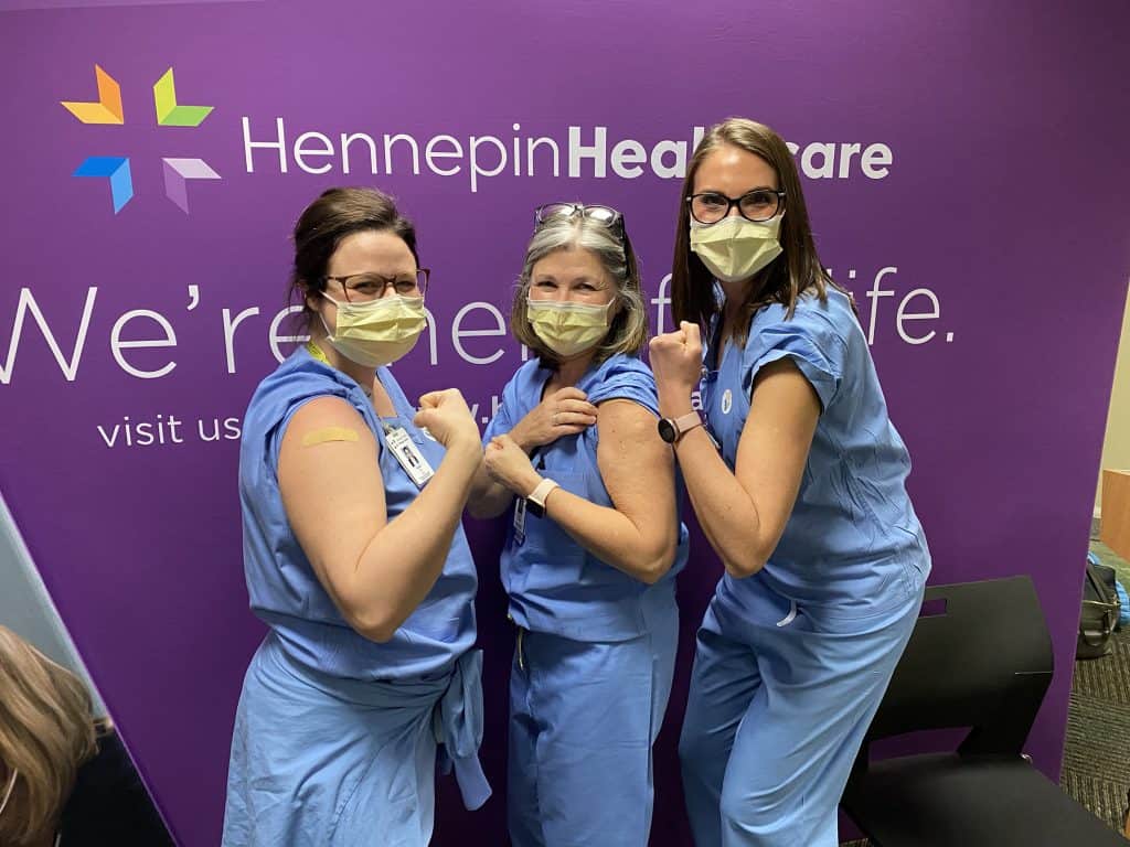 three masked employees showing their arm where they got the vaccine