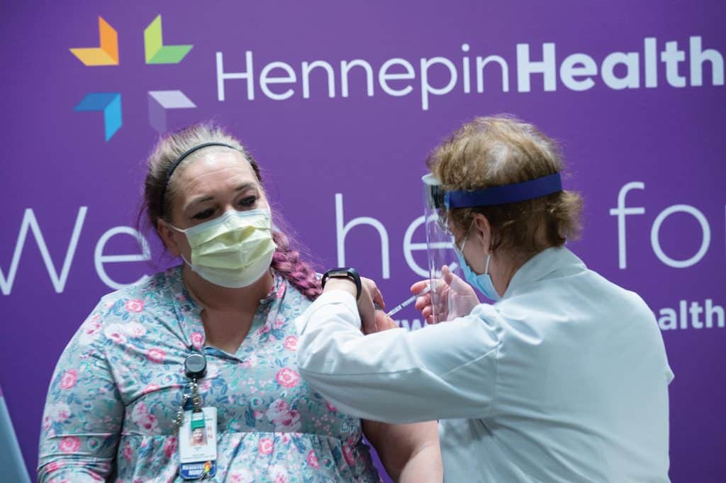 masked employee receiving vaccine from masked nurse