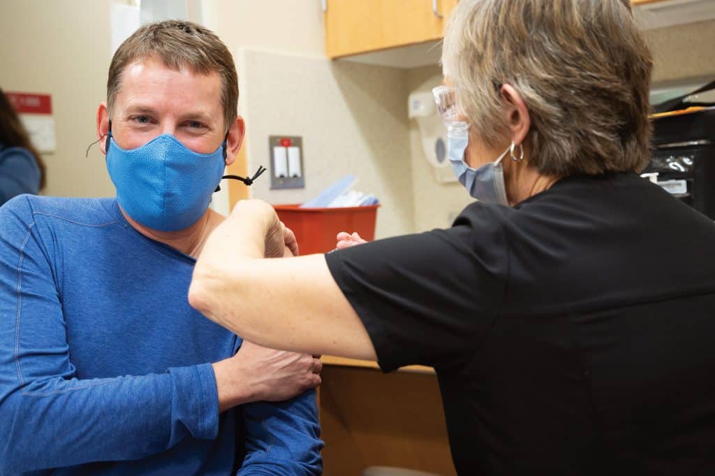masked employee receiving vaccine from masked nurse