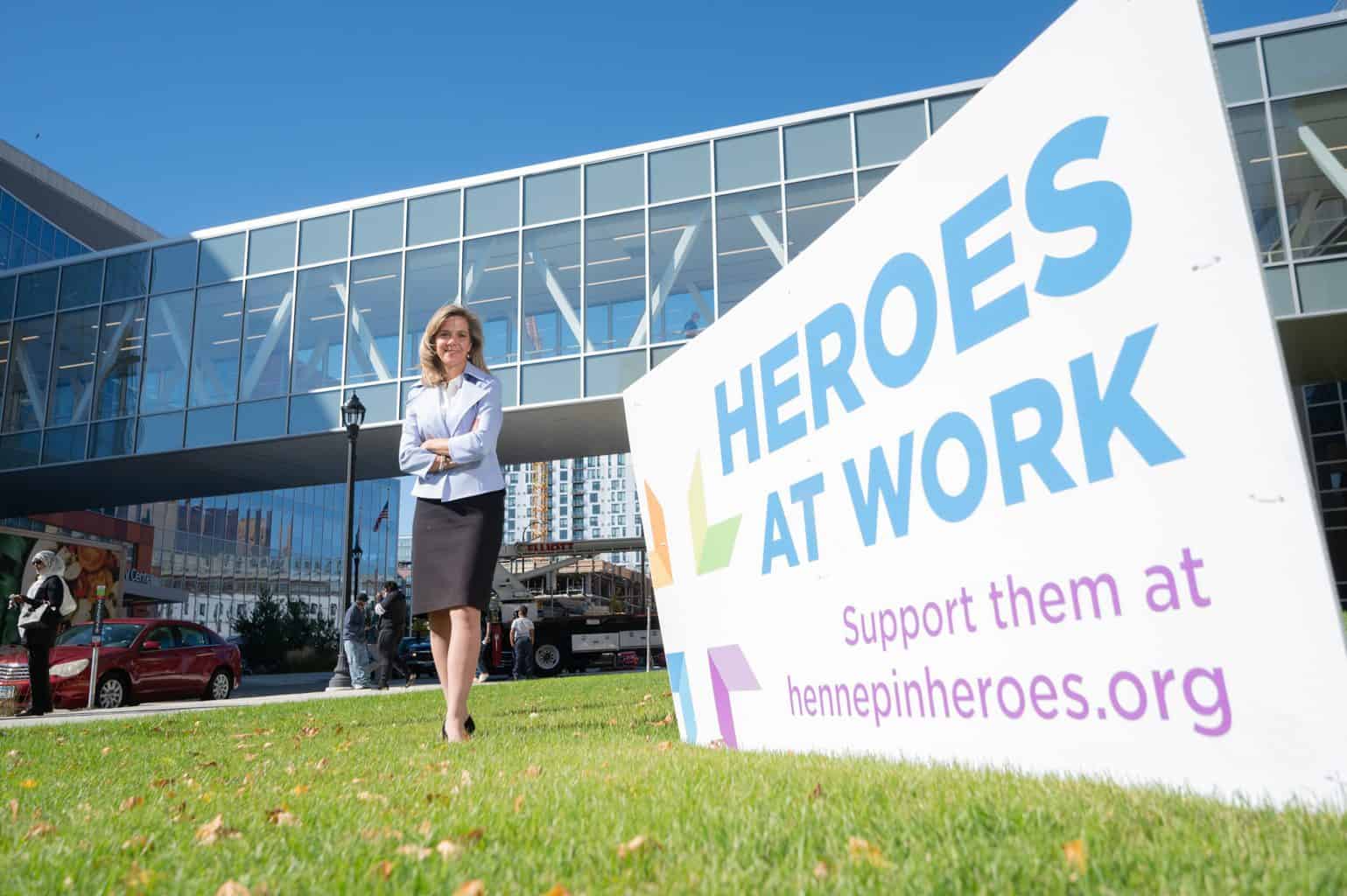 ceo jennifer decubellis standing next to heroes at work sign with skyway in background spring