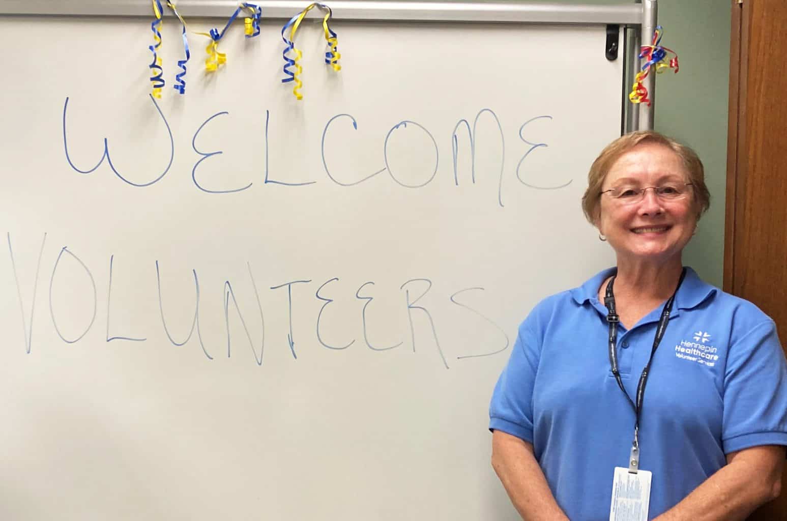 female volunteer smiling in front of board that says welcome