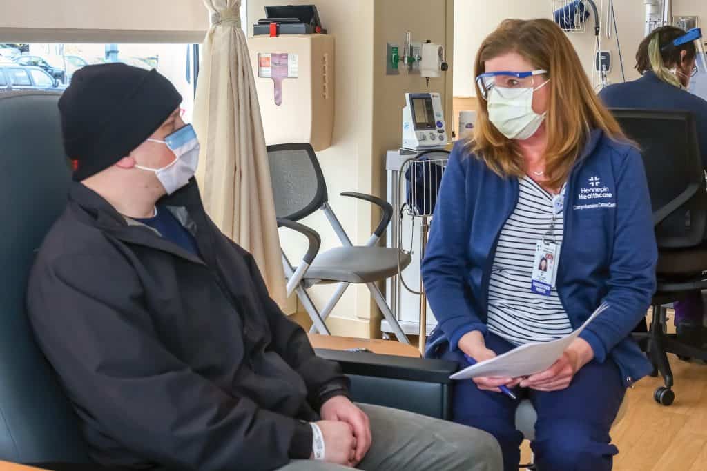 seated nurse talking to male patient in cancer center wearing masks