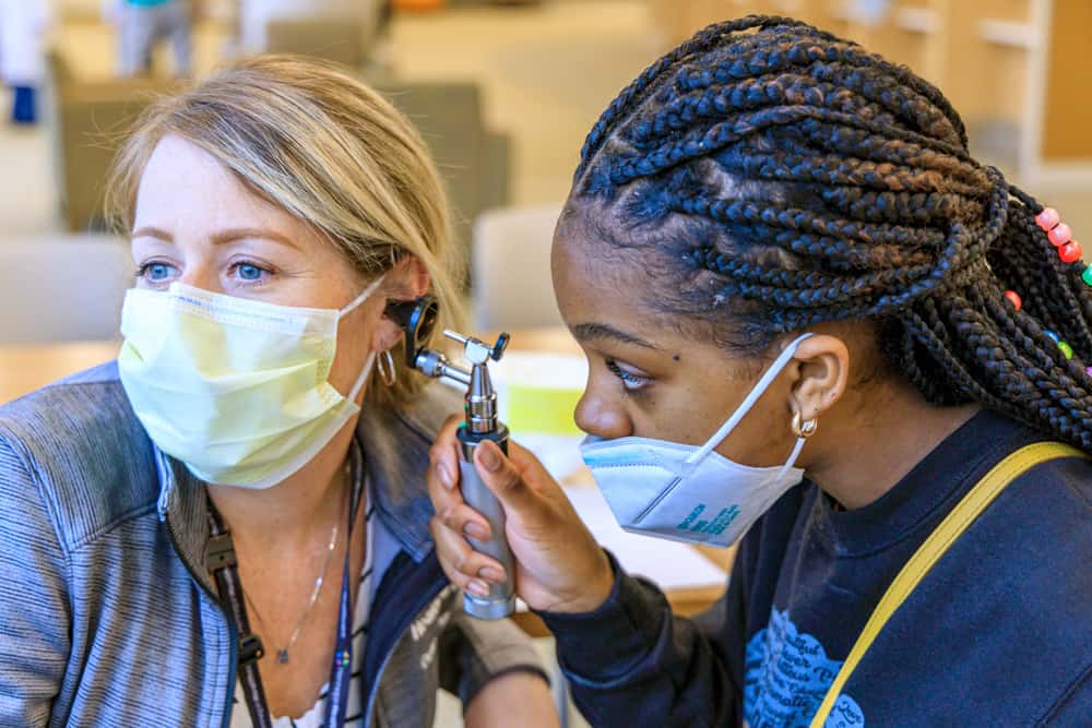 masked black medical student doing ear exam on masked provider