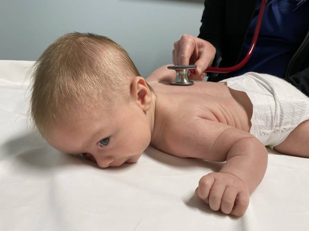 baby on exam table with doctor listening to heart with stethoscope
