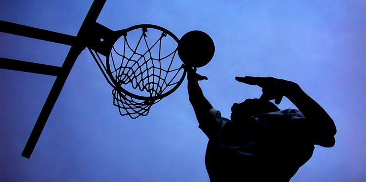 Stunning silhouette of basketball player and hoop against deep blue sky.  If there was one shot he could make, it was a finger roll.