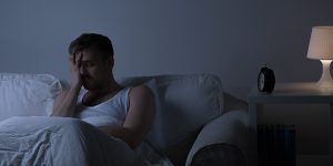 man sitting in the dark on the couch who cannot sleep, 10 steps for managing sleep during the COVID-19 pandemic, sleep disorders during covid, symptoms of depression or anxiety, difficulty concentrating, sleep issues, mark rosenblum