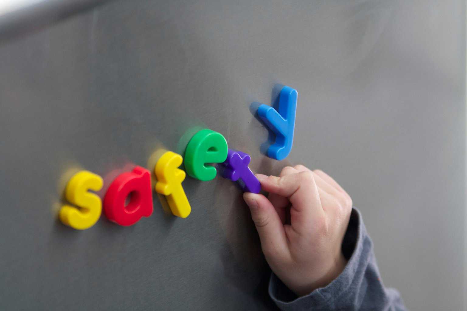 Small hand using colorful magnets to spell safety