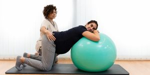 A Pregnant Woman Doing Breathing Exercises And Resting On A Fitness Ball With The Help Of Her Physiotherapist