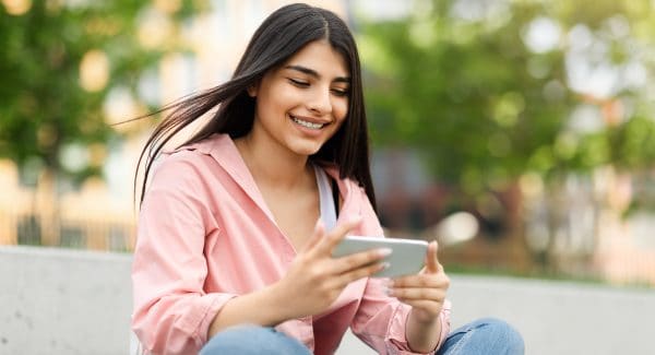 Smiling Teen Hispanic Lady Messaging Or Playing On Smartphone While Relaxing In Park Outdoors, Free Space, mychart