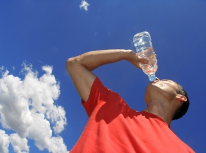 young man drinking water with a blue sky behind him, Be prepared for hot weather, life-threatening medical conditions, hyperthermia, heat stroke, stay cool, Drink plenty of water