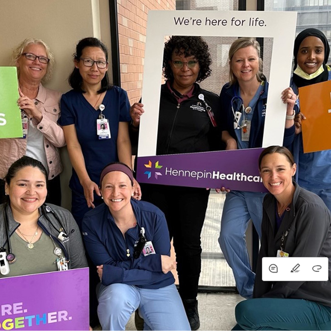 Hennepin Healthcare team members in a happy group photo holding signs to express employee pride